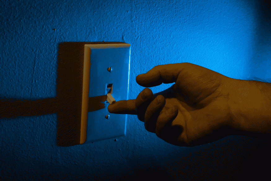 Hand schaltet Lichtschalter aus, um Stromverbrauch und Nebenkosten zu senken