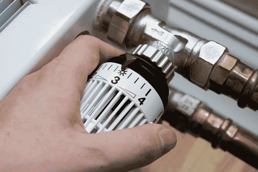 Hand dreht Thermostat am Heizkörper herunter, um Heizkosten zu sparen
