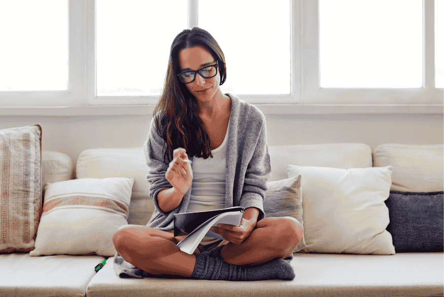 Junge Frau sitzt entspannt auf dem Sofa und reflektiert mit einem Notizbuch – symbolisiert die bewusste Reflexion als Teil der 7-Tage-Regel für bessere finanzielle Entscheidungen.