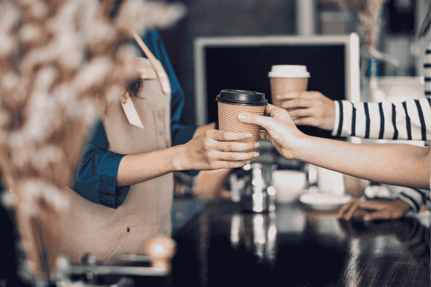 Nahaufnahme einer Barista, die einen Coffee-to-go überreicht – symbolisiert spontane Ausgaben im Alltag, die oft unbemerkt das Monatsbudget belasten.