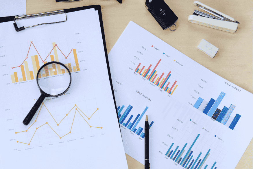 Schreibtisch mit Finanzberichten, Lupe und Diagrammen – symbolisiert die gezielte Analyse kleiner Ausgaben zur Wiedererlangung der finanziellen Kontrolle im digitalen Alltag.