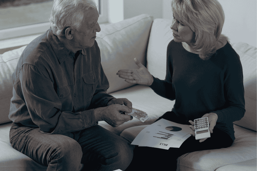 Älteres Paar sitzt auf dem Sofa und spricht über Finanzen – mit Kreditkarte, Taschenrechner und Rechnungen in der Hand. Symbolisiert offene, vertrauensvolle Geldgespräche ohne Scham.