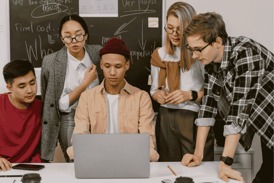 Gruppe junger Erwachsener bespricht gemeinsam etwas am Laptop – symbolisiert die Notwendigkeit klarer Absprachen bei Gruppengeschenken und gemeinschaftlichen Ausgaben.