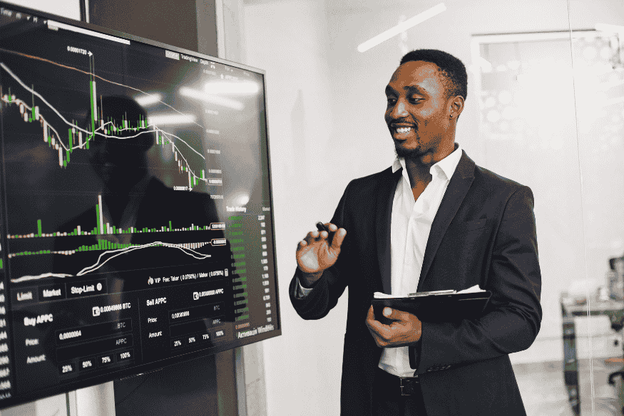 Ein Mann im Anzug präsentiert ein Finanzdiagramm auf einem digitalen Bildschirm, das Marktbewegungen zeigt, und erklärt wirtschaftliche Trends in einer Büroumgebung.