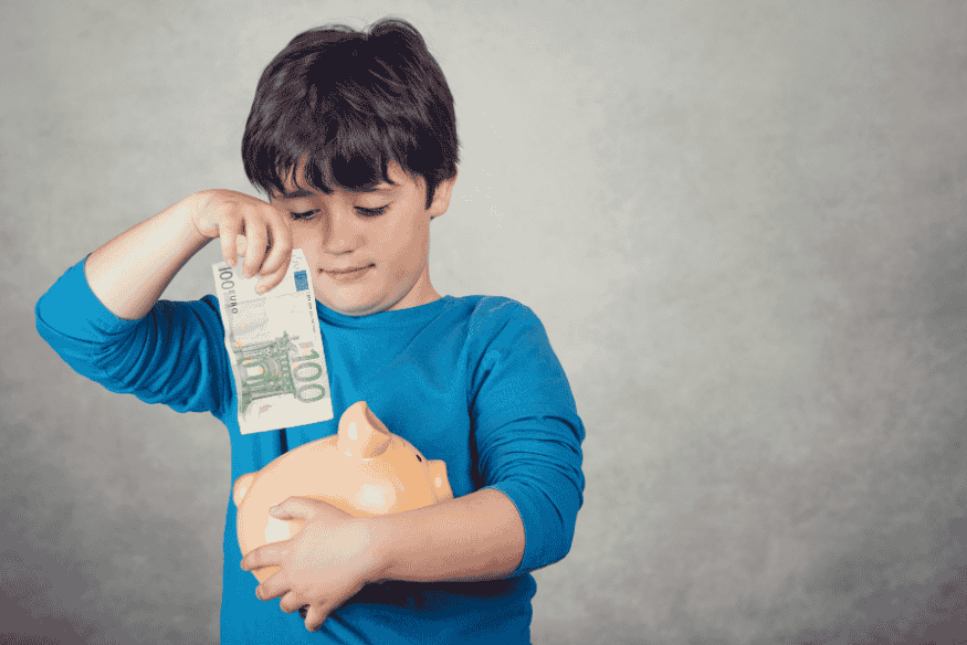 Junge steckt Geldschein in Sparschwein, um für große Anschaffungen wie Auto oder neue Küche zu sparen